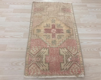 May include: A rectangular, vintage-style rug with a central geometric design in shades of pink, beige, and brown. The rug features a distressed look, with a faded appearance and fringed edges. The pattern includes a central cross-like motif.