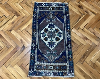 Op de afbeelding: Een rechthoekig, vintage tapijt met een centraal medaillonontwerp. Het tapijt heeft een donkerblauwe rand met ingewikkelde patronen, rondom een centraal veld van bruin en wit met bloemmotieven. Het tapijt is ongeveer 61 cm lang en 30 cm breed.