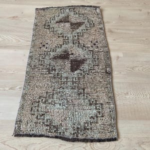 May include: A vintage rug with a geometric pattern in shades of brown and beige. The rug has a fringed edge and is made of a woven material.