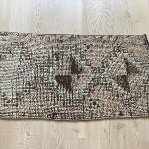 May include: A brown and beige patterned rug with a geometric design. The rug has a fringed edge and is made of a woven material.