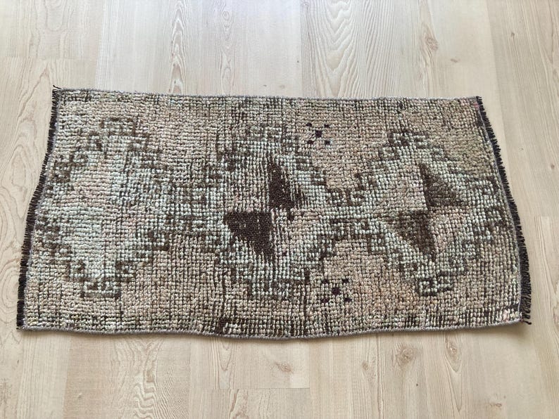 May include: A brown and beige patterned rug with a geometric design. The rug has a fringed edge and is made of a woven material.