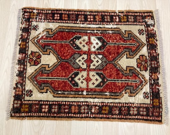 May include: A rectangular, hand-woven rug with a central geometric design in shades of red, beige, and brown. The rug features a detailed border and fringe along the edges. The rug's dimensions are approximately 24 inches by 36 inches.
