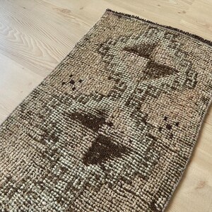 May include: A brown and beige patterned rug with a geometric design. The rug has a distressed look and is made of woven fibers.