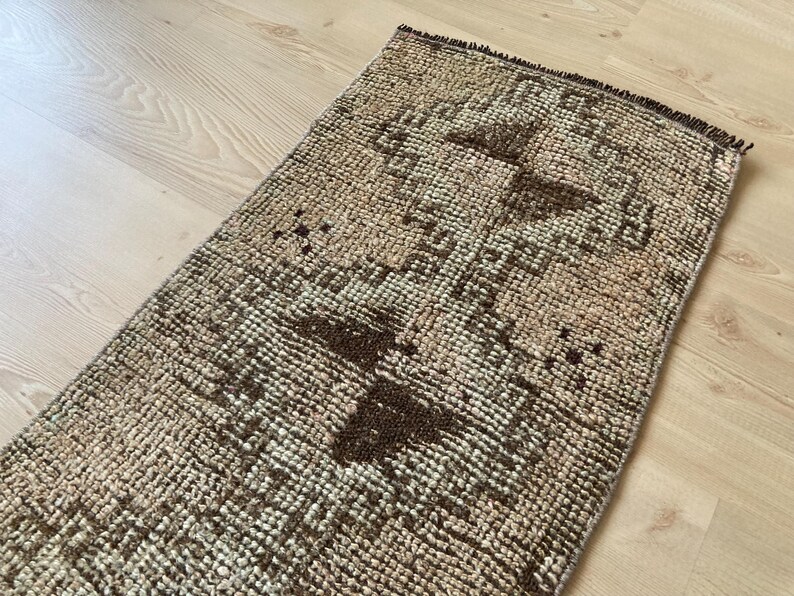 May include: A brown and beige patterned rug with a geometric design. The rug has a distressed look and is made of woven fibers.