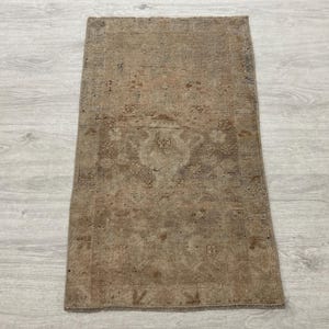 Puede incluir: Una alfombra rectangular con una paleta de colores marrón y bronceado descoloridos y apagados. La alfombra muestra un patrón tejido tradicional e intrincado con un motivo de medallón central y un borde, con una textura desgastada.