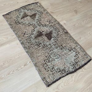 May include: A vintage style runner rug with a geometric pattern in shades of brown, beige, and white. The rug has a distressed look and is made of a soft, woven material.