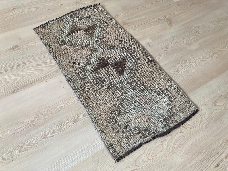 May include: A vintage style runner rug with a geometric pattern in shades of brown, beige, and white. The rug has a distressed look and is made of a soft, woven material.