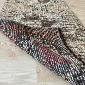 May include: A vintage rug with a faded, distressed pattern in shades of brown, beige, and pink. The rug has a woven texture and a fringed edge.