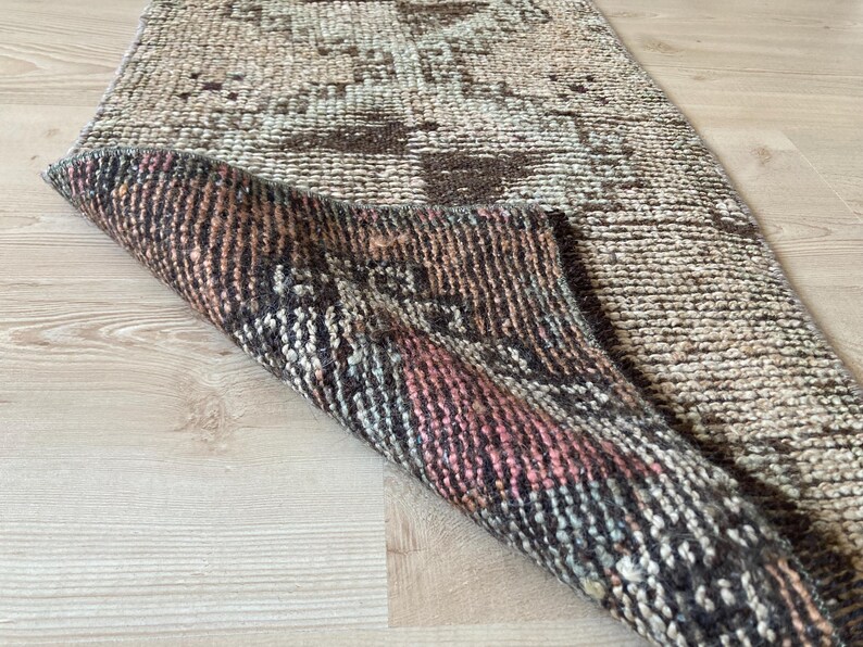 May include: A vintage rug with a faded, distressed pattern in shades of brown, beige, and pink. The rug has a woven texture and a fringed edge.
