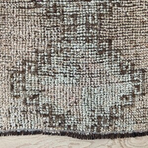 May include: A close-up of a brown and cream patterned rug with a fringe border. The rug has a distressed, vintage look.