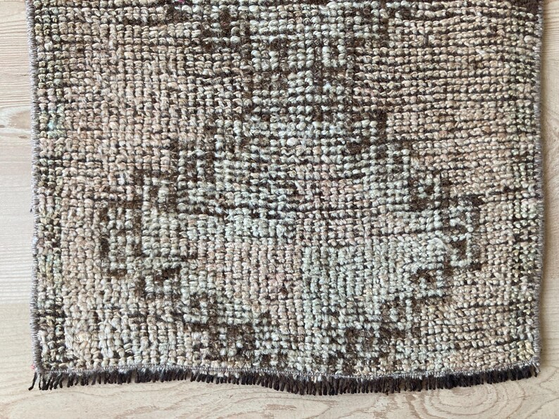 May include: A close-up of a brown and cream patterned rug with a fringe border. The rug has a distressed, vintage look.