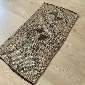May include: A small, rectangular rug with a brown and beige geometric pattern. The rug has a distressed, vintage look.