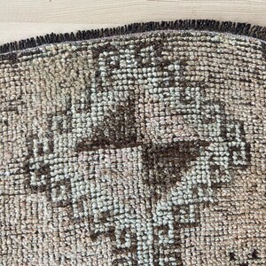 May include: A close-up of a brown and cream patterned rug with a fringe border. The rug has a geometric design with a central cross shape.