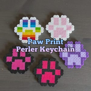 May include: Five colorful paw print keychains made with Perler beads. The keychains are in rainbow, pink, black and pink, red and black, and purple colors.