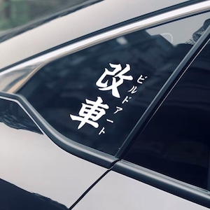 May include: A white vinyl sticker with Japanese characters that read "改車" (Kaizosha) which means "modified car" in English. The sticker is on the back window of a black car.