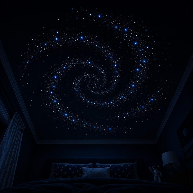 Op de afbeelding: Een donker slaapkamerplafond is versierd met een spiraalvormige melkweg van kleine, helderblauwe sterren. De kamer heeft een bed met kussens met patronen en een nachtlampje, wat een hemelse sfeer cre&euml;ert.