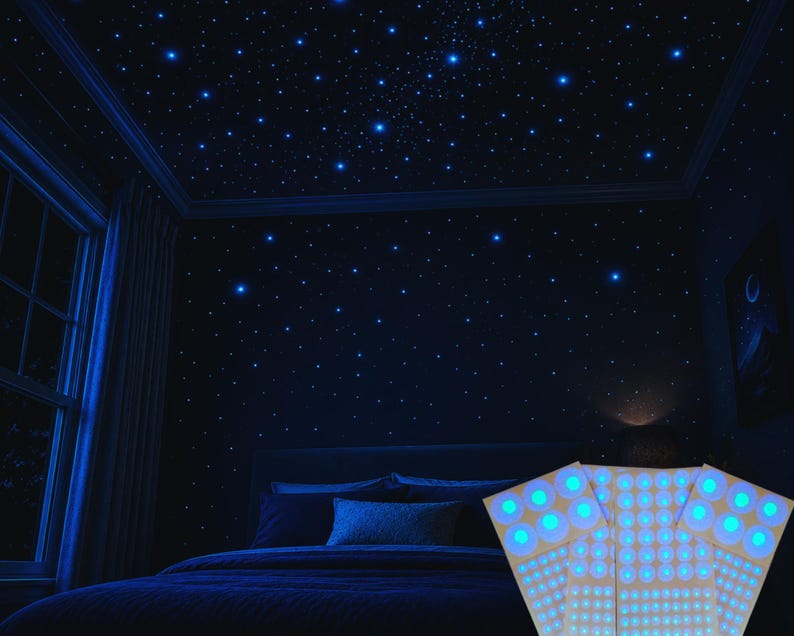 Op de afbeelding: Een slaapkamer met een donkerblauw kleurenschema, met een bed, een raam en een plafond versierd met gloeiende blauwe sterstickers. De kamer is zwak verlicht en cre&euml;ert een hemelse sfeer. Een decoratief licht staat op de voorgrond.