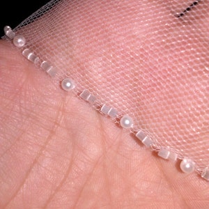 May include: White tulle fabric with a row of small white beads sewn along the edge.