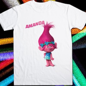 May include: White t-shirt with a pink troll character wearing a blue dress and a flower crown. The text "AMANDA" is printed on the shirt.