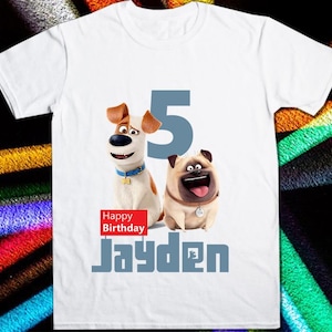 以下が含まれることがあります： 白地に、茶色と白の犬と茶色のパグの2匹の犬の漫画の画像が描かれたTシャツ。犬の後ろには数字の5が描かれている。犬の下には「Happy Birthday Jayden」の文字が書かれている。