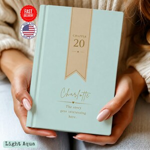 May include: A light aqua hardcover book featuring a vertical tan banner with the text "CHAPTER 20" in gold. Below the banner, the name "Charlotte" is printed in gold script, followed by the text "The story gets interesting here."