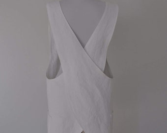 May include: White linen apron with a criss-cross back design and two pockets. The apron is on a wooden mannequin.