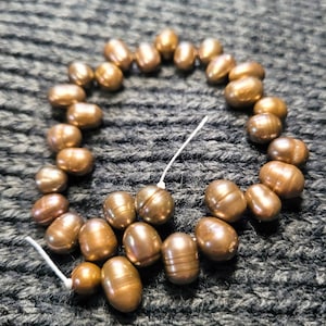 May include: A strand of brown pearls with a few pearls scattered around it. The pearls are arranged in a circle on a gray knitted surface.