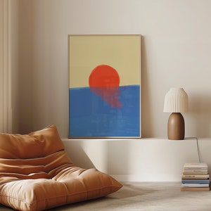 Könnte beinhalten: Ein gerahmter abstrakter Druck eines roten Sonnenuntergangs über einem blauen Meer. Der Druck hängt an einer weißen Wand über einem braunen Ledersessel.