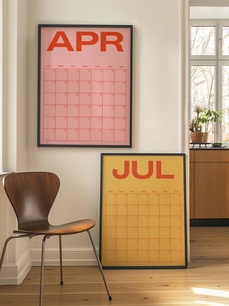 May include: Two framed wall calendars, one pink with "APR" in orange, the other yellow with "JUL" in orange. Both have a grid layout for dates. A wooden chair with metal legs is in the foreground.
