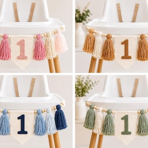 May include: A high chair banner featuring a central off-white fabric pennant with the number 1 in various colors, flanked by wooden beads and yarn tassels. Four color variations are shown: pink, brown, blue, and green, each with matching tassels.