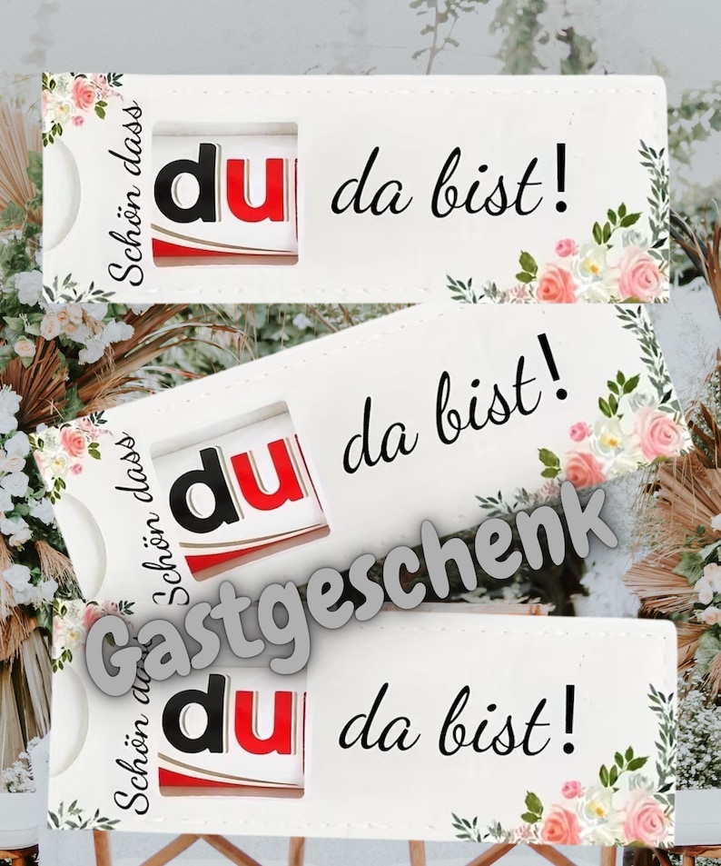 May include: White gift card holders with floral accents and the text "du da bist!" in black. The holders feature a cutout revealing a red and white product. The word "Gastgeschenk" is also visible.