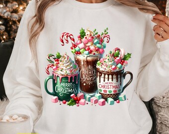 Peut inclure: Un sweat-shirt blanc à manches longues avec un motif de trois tasses remplies de chocolat chaud, crème fouettée, sucres d'orge et guimauves. La tasse verte indique Merry Christmas, la blanche Merry Christmas et le verre central Chiao Grier.