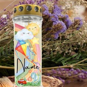 May include: A cylindrical glass memorial candle with a gold-colored metal lid. The exterior features a colorful graphic print of a smiling sun, a cloud, a rainbow, a kite, a red car, and a bucket, with the word Name printed in black script.