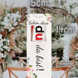 May include: A white rectangular gift tag, 5.5 inches long and 2 inches wide, with the German text "Sch&ouml;n dass du da bist!" and floral accents. The tag features a cutout revealing the letters "du" in red and black.