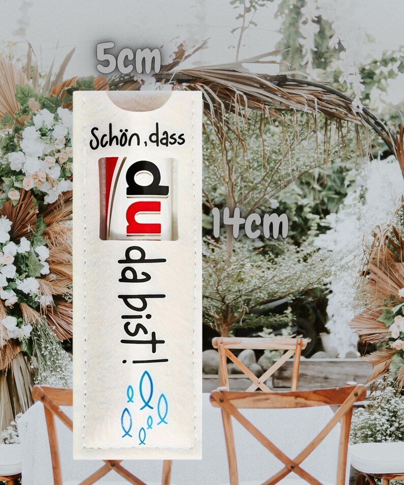 May include: A rectangular, off-white fabric item, 5 cm wide and 14 cm tall, with German text and a graphic. The text reads "Sch&ouml;n, dass du da bist!" in black, with a red and black graphic. Blue fish icons are at the bottom.