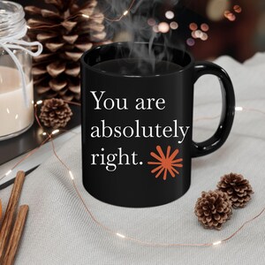 Könnte beinhalten: Ein schwarzer Keramikbecher mit dem weißen Text "You are absolutely right.", gefolgt von einer kleinen, rostfarbenen Sternchengrafik. Der Becher hat einen Standardhenkel und ist mit einem Heißgetränk gefüllt, das oben sichtbar dampft.