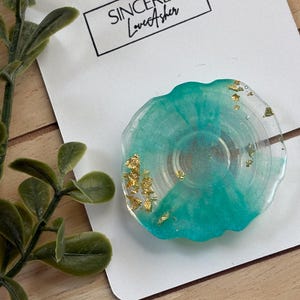 Puede incluir: Un posavasos de resina transparente con un dise&ntilde;o turquesa y hojas de oro. El posavasos tiene una forma org&aacute;nica y presenta el texto "Sincerely Love Asher" en una tarjeta blanca.