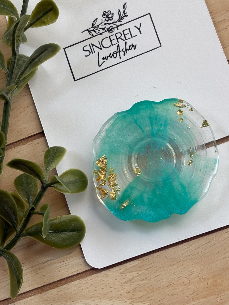 Puede incluir: Un posavasos de resina transparente con un dise&ntilde;o turquesa y hojas de oro. El posavasos tiene una forma org&aacute;nica y presenta el texto "Sincerely Love Asher" en una tarjeta blanca.