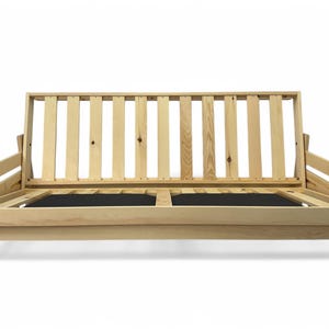 K&ouml;nnte beinhalten: Ein hellfarbiger Futonrahmen aus Holz mit Lattenr&uuml;cken und Armlehnen. Der Rahmen hat ein schlichtes, modernes Design und verf&uuml;gt &uuml;ber eine schwarze Basis. Der Futon ist so konzipiert, dass er sich in ein Bett verwandeln l&auml;sst.