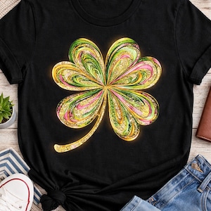 May include: Black t-shirt featuring a vibrant, four-leaf clover design. The clover is rendered in shades of green, pink, and gold, with a glittery texture. The shirt is styled with denim shorts and white sneakers, suggesting casual wear.