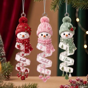 May include: Three hanging snowman ornaments with knit-style hats and scarves in red, pink, and sage green. Each snowman features a white spiral ribbon base personalized with the names Keith, Mabel, and Elton, accented with small charms.