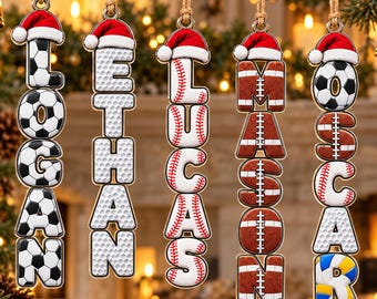 May include: Five vertical hanging ornaments featuring names spelled out in sports-themed letters topped with red and white Santa hats. The names Logan, Ethan, Lucas, Mason, and Oscar are displayed using soccer ball, golf ball, baseball, football, and volleyball patterns.