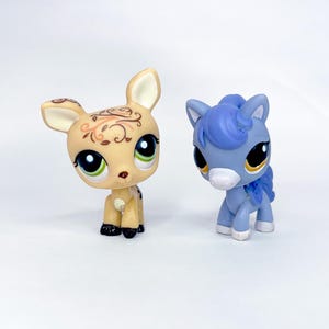 May include: Two collectible figurines: a tan deer with brown floral accents and a blue pony with a white muzzle. Both have large, expressive eyes and are set against a white background. The deer has black hooves, and the pony has white hooves.