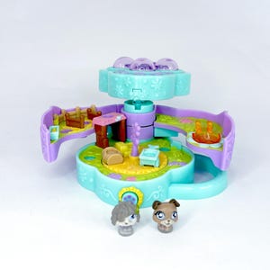 May include: A colorful, miniature playset with a flower-shaped base, featuring a rotating top with translucent purple domes. The playset includes small animal figurines and miniature furniture. The color scheme includes shades of blue, purple, green, and yellow.