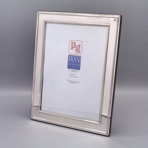 Op de afbeelding: Zilveren fotolijst met een afgeschuinde rand en een witte passe-partout. De lijst heeft een label met de tekst "Pg Miani Venezia".