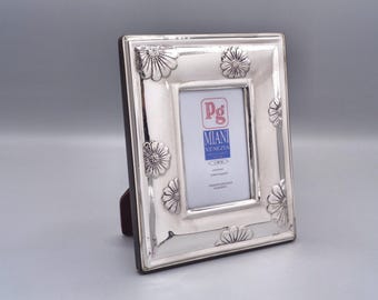 May include: Silver picture frame with a floral design and a small rectangular opening for a photo. The frame has a stand on the back and the text "Pg Miani Venezia" is visible in the opening.