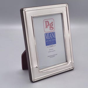 Op de afbeelding: Zilveren fotolijst met een rood en blauw label met de tekst "Pg Miani Venezia Artigiani in Argento".