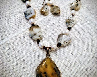 May include: A necklace and earring set featuring large, irregular-shaped stones in shades of white, tan, and brown, interspersed with small pearls and dark beads. The necklace has a pendant with a large, amber-colored stone.