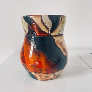 Può includere: Un vaso in ceramica con un design astratto unico. Il vaso presenta una combinazione di colori, tra cui arancione, verde scuro, beige e marrone. La finitura lucida esalta le tonalità vibranti, creando un pezzo decorativo sorprendente. Il vaso ha un corpo arrotondato.