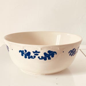 May include: Cream ceramic bowl featuring a blue floral pattern. The bowl has a scalloped rim and a decorative blue design around the exterior. Likely used for serving or mixing, it's a classic kitchenware item.